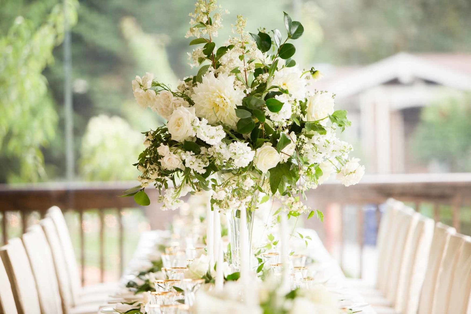 Tall white-and-greenery centerpiece on a candlelit reception table