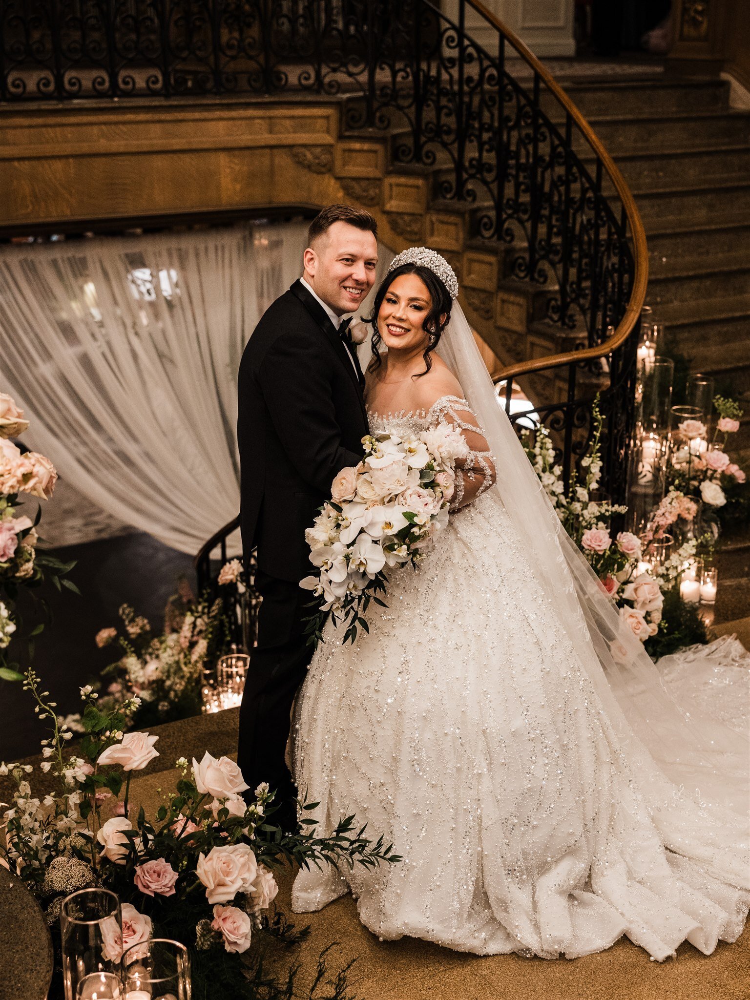 Bride and groom on a grand staircase with a cascading blush bouquet